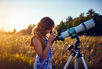Ein Mädchen schaut durch das Teleskop um das Universum zu erkunden.