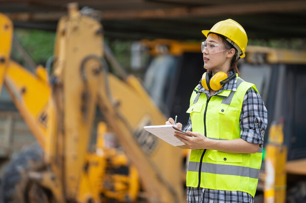 Eine junge Frau mit Helm und Warnweste ist auf einer Baustelle.
