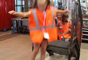 Schülerinnen springen in orangenen Warnwesten von einer Rampe