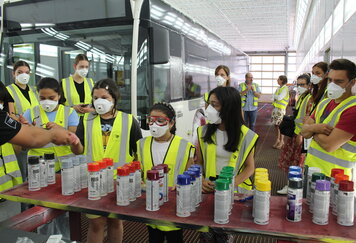 Schülerinnen stehen mit Schutzmasken vor Farbspraydosen