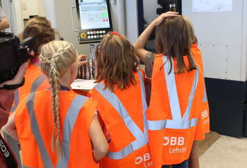 Schülerinnen stehen in orangenen Warnwesten vor CNC Maschine