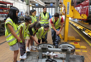 Lehrling zeigt Schülerinnen Reifen in einer Werkstatt